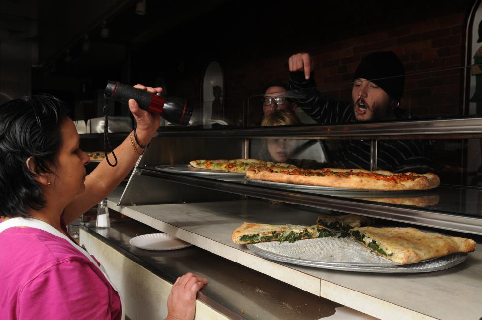 Anna Romaro shines a flashlight on the pizza options so customers can choose slices at Pinnocchio's on Main Street in Northampton, where pizza was made Sunday despite the power outage. CAROL LOLLIS -