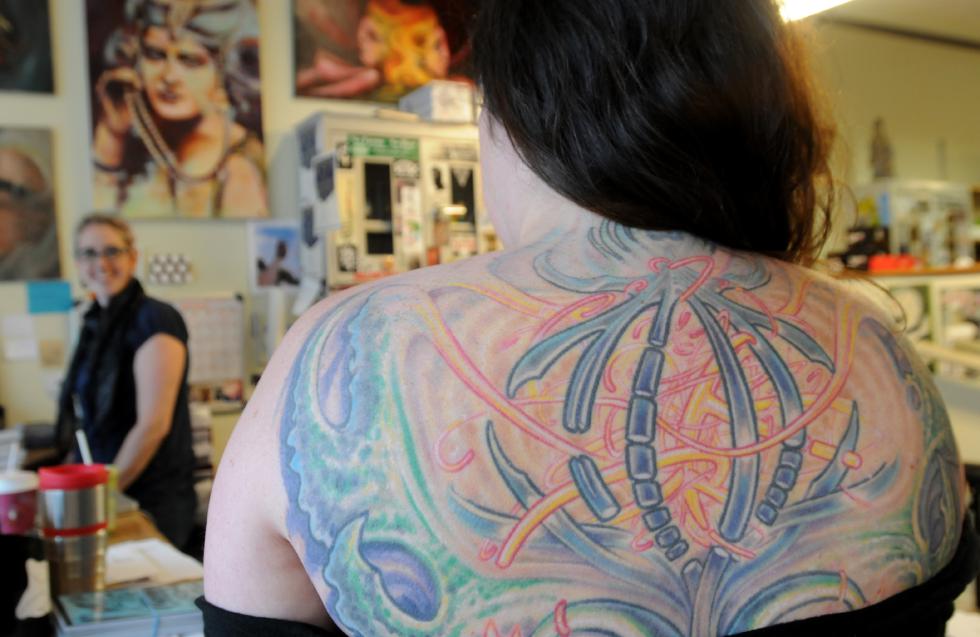 CAROL LOLLIS left, Rachael Nalewanski, and Mary Bowen, employees of Off the Map Tattoo. Bowen shows a portion of the tattoo that fills her back. - Carol Lollis | Daily Hampshire Gazette