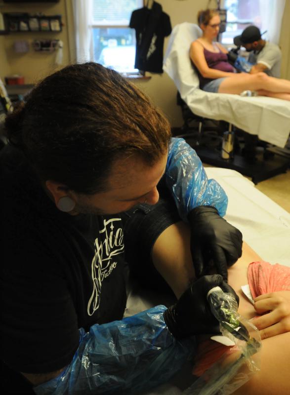 CAROL LOLLIS left, Josh Suchoza, an employee at Off the Map Tattoo, works on an elephant tattoo on Lauren Langione. In the back ground is Breanne Ryan receiving a tattoo by Andre Cheko. - Carol Lollis | Daily Hampshire Gazette