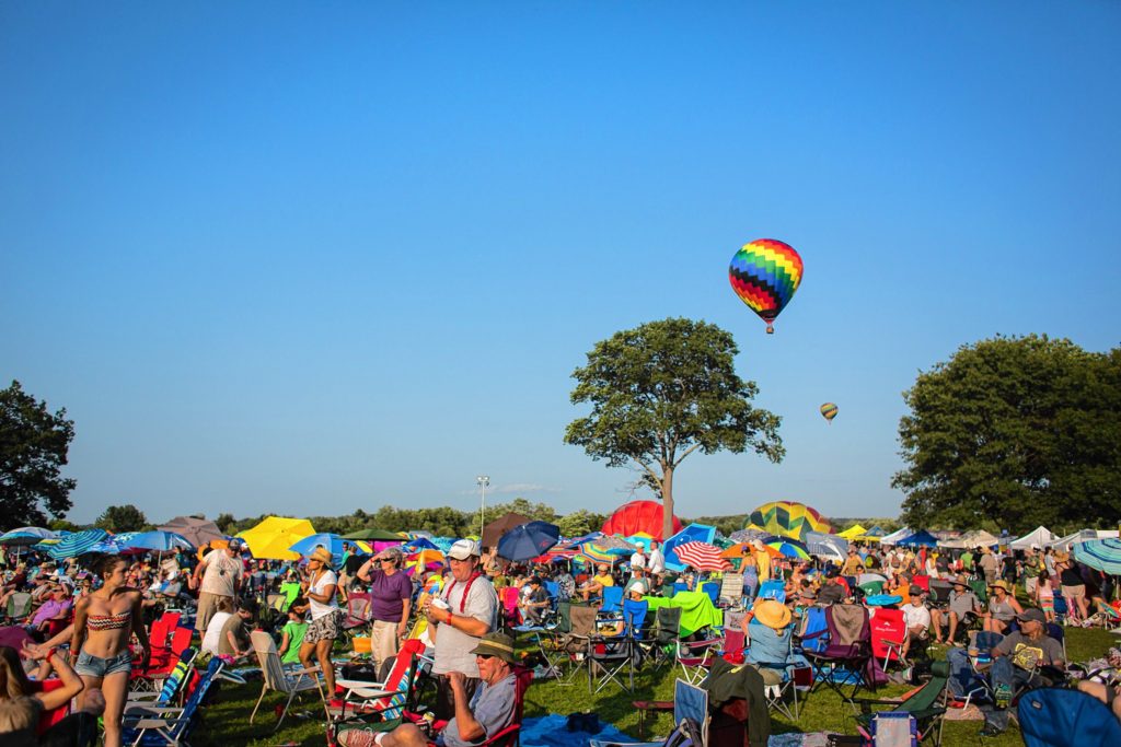 Hot air balloons lift off behind a field filled with attendees of the Green River Festival on the campus of Greenfield Community College, Saturday July 11. Recorder/Matt Burkhartt