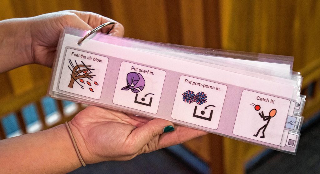 Lauren Boyce, who is the operations manager at Holyoke Children's Museum, displays one of several communication boards used to help children understand Sensory Sundays activities, Friday, Oct. 25, 2019 at the museum. This one is for A-Mazing Airways, where pompoms or scarves are placed in transparent tubes and move through them on air currents until they are discharged.