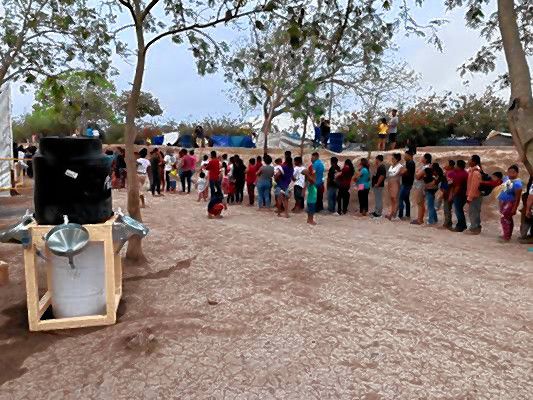 Asylum seekers lined up for food with a handwashing station nearby. 