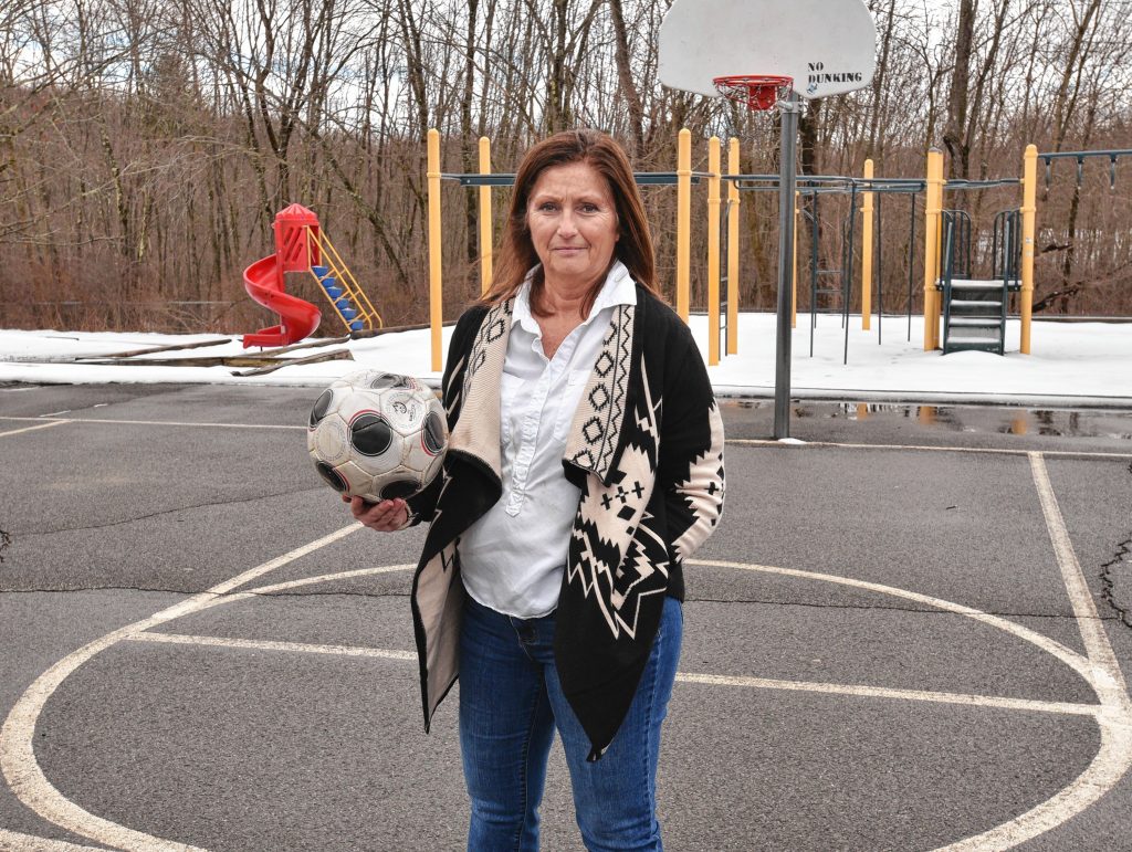 Jean Fay, who is a special education paraeducator at Crocker Farm School in Amherst, stands on the school's empty playground, Tuesday, Mar. 24, 2020. She said her students liked to play soccer there.