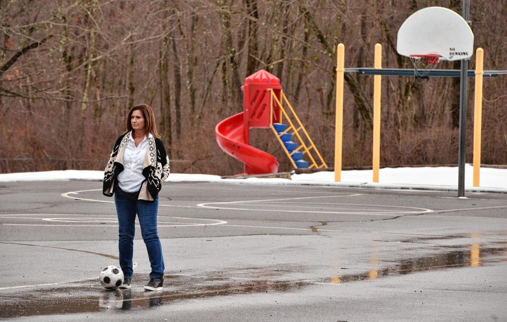 Jean Fay, who is a special education paraeducator at Crocker Farm School in Amherst, stands on the school's empty playground, Tuesday, Mar. 24, 2020. She said her students liked to play soccer there.
