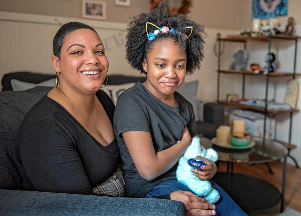 Emily Collins and her daughter, Gabrielle Collins-Hill, 8, pose in their Holyoke home with an urn containing the ashes of her son, Sebastian, who died in 2018 at the age of 2 weeks. Photographed on Wednesday, March 18, 2020.