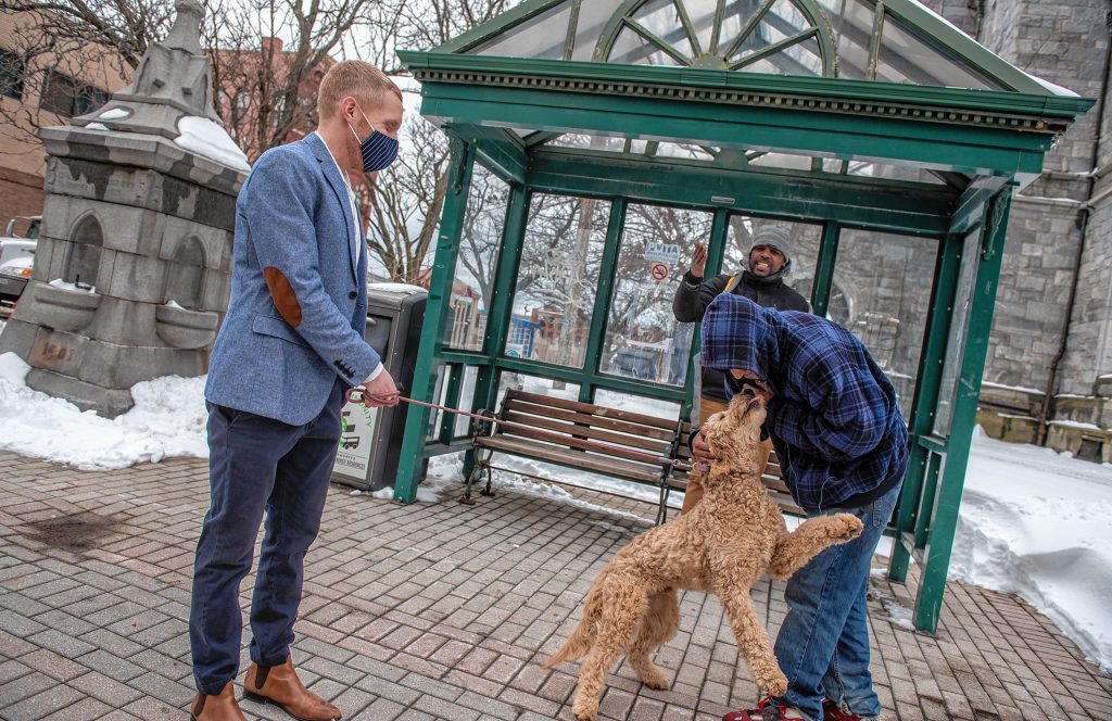 Holyoke Mayor Alex Morse greets residents Abram Marshall, foreground, and Antwon Davis at the bus stop outside city hall while walking his dog, Oliver, a six-month-old labradoodle, on Thursday, Feb. 4, 2021.