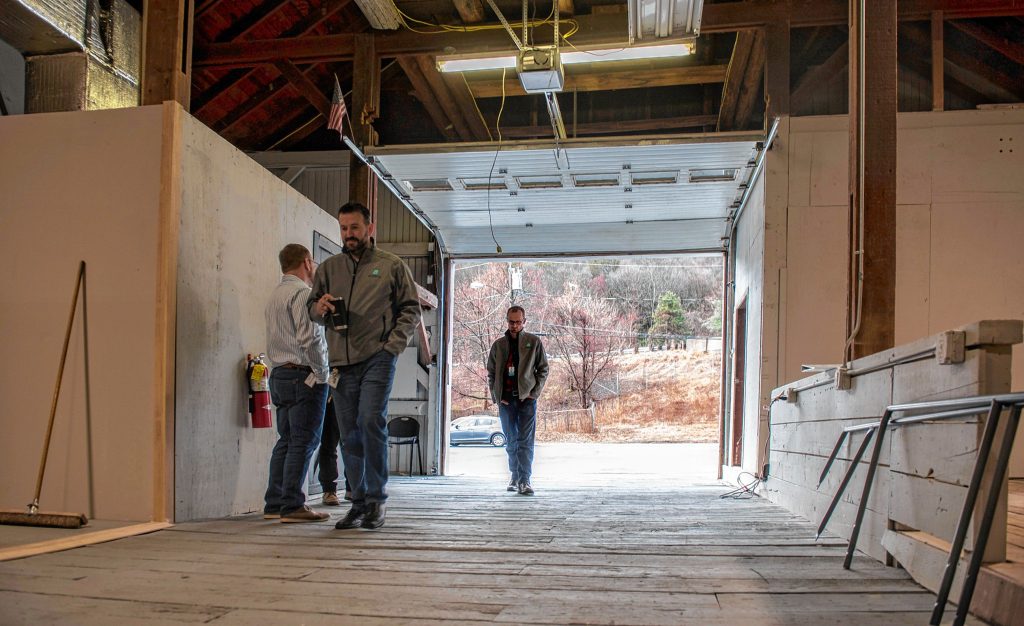 Budzee CEO Kevin Perrier, far left, COO Volkan Polatol and consultant Ezra Parzybok, right, walk through the sally port of their Easthampton warehouse, once a working barn for the former Underwood Farm, on Friday, April 8, 2022. With a remotely controlled door, the garage allows delivery vehicles to be loaded and unloaded in a secure space, a requirement of the Cannabis Control Commission.