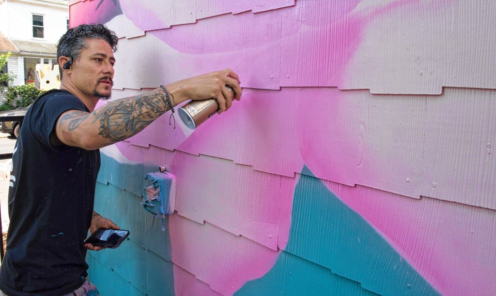 Los Angeles artist Ryan Sarfati,  who goes by the artistic name Yanoe — pronounced “ya know” — works on a painting of a dragon on a home on Cottage Street in Easthampton.