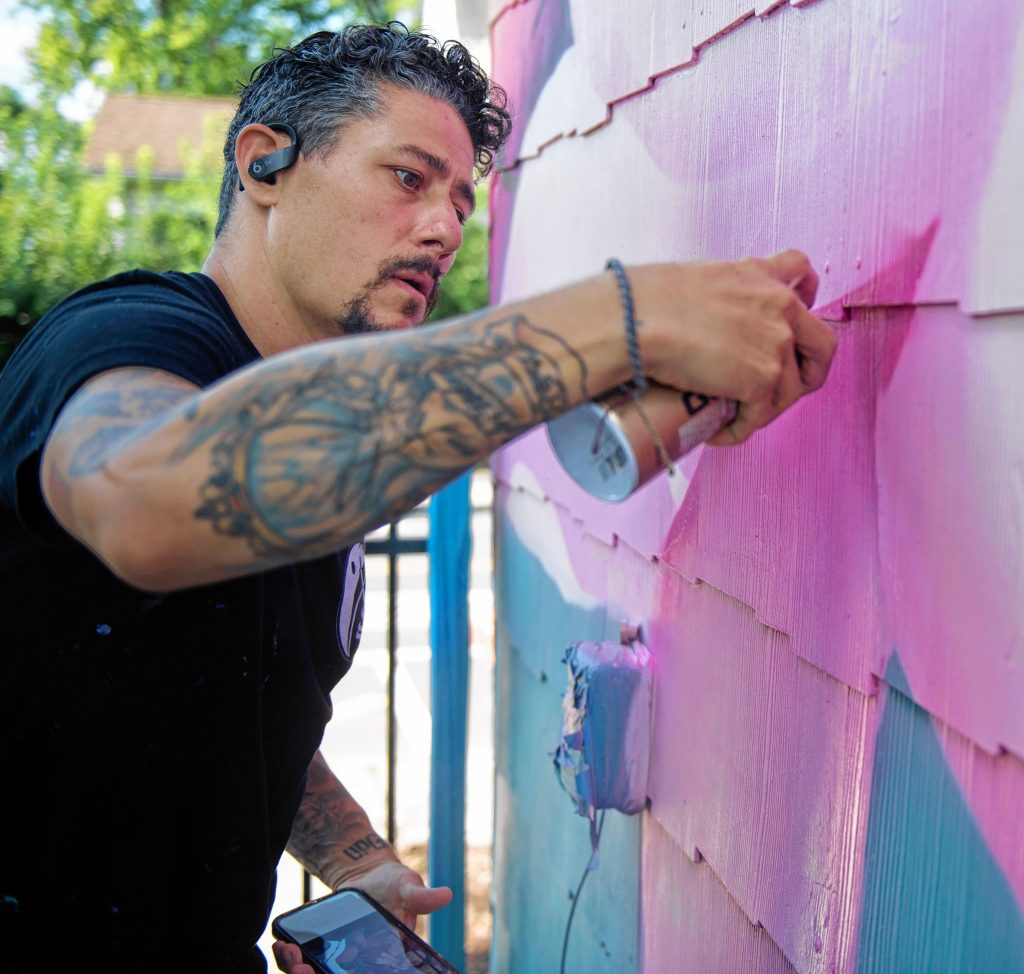 Los Angeles artist Ryan Sarfati,  who goes by the artistic name Yanoe — pronounced “ya know” — works on a painting of a dragon on a home on Cottage Street in Easthampton. The painting is wedding anniversary gift from Easthampton resident Stephen Parmenter to his  wife Nina.