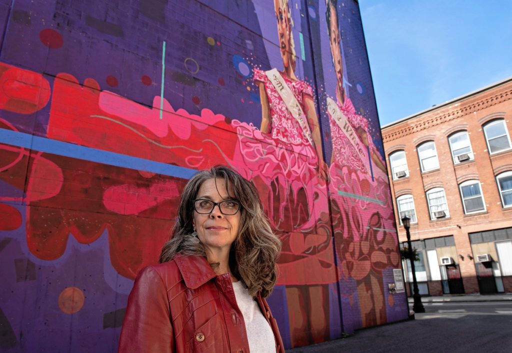 Britt Ruhe, the director of the Commonwealth Murals in Springfield, stands in front of a mural called Victoria painted by Andrae and Priya Green on Taylor Street,  one of the 36 murals in town.