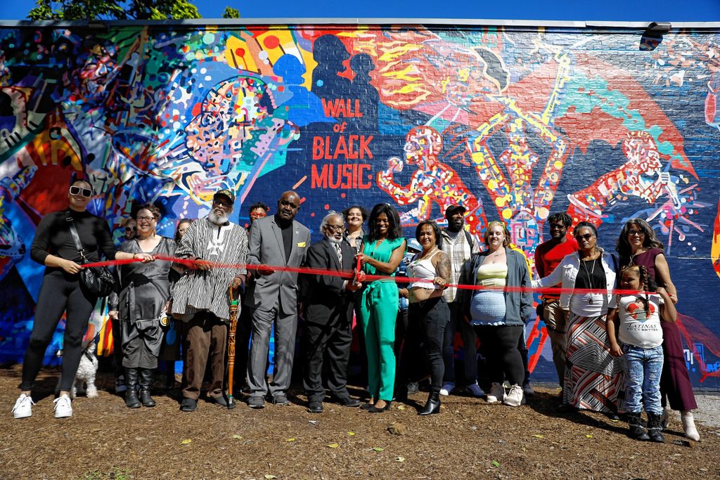 The ribbon is cut on Saturday afternoon for the unveiling of The Wall of Black Music mural, originally created by Nelson Stevens with his student Clyde Santana, that was recreated by Common Wealth Murals and the Community Mural Institute and is now on view at 1 Montrose Street in Springfield.