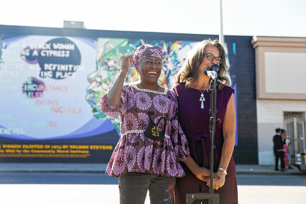 Rosemary Tracy Woods, left, and Britt Ruhe speak Saturday afternoon during the commemoration ceremony of the Tribute to Black Women mural, originally created by her father Nelson Stevens in 1974, that was recreated by Common Wealth Murals and the Community Mural Institute and is now on view at 38 Catherine Street in Springfield.