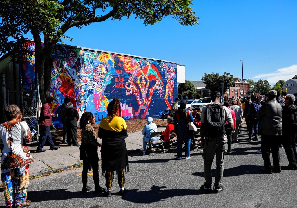 People gather on Saturday afternoon for the commemoration ceremony of The Wall of Black Music mural, originally created by Nelson Stevens with his student Clyde Santana, that was recreated by Common Wealth Murals and the Community Mural Institute and is now on view at 1 Montrose Street in Springfield.